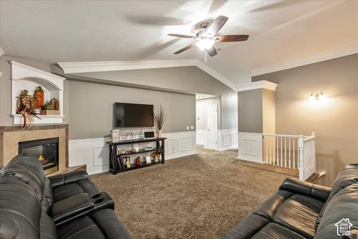 Vaulted ceilings featuring crown molding, a built-in fireplace with tile surround and arched alcove, chair rail wainscoting, and a ceiling fan