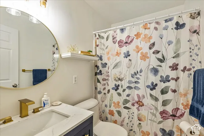 Bathroom featuring a stone-composite countertop with an integrated rectangular basin, gold-finish faucet, circular gold-rimmed wall mirror, and navy blue vanity cabinetry
