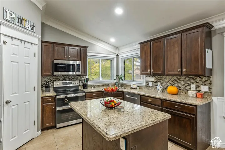Kitchen featuring dark wood cabinetry, a center island with a stone-composite countertop, a multi-tonal mosaic tile backsplash, and stainless steel appliances