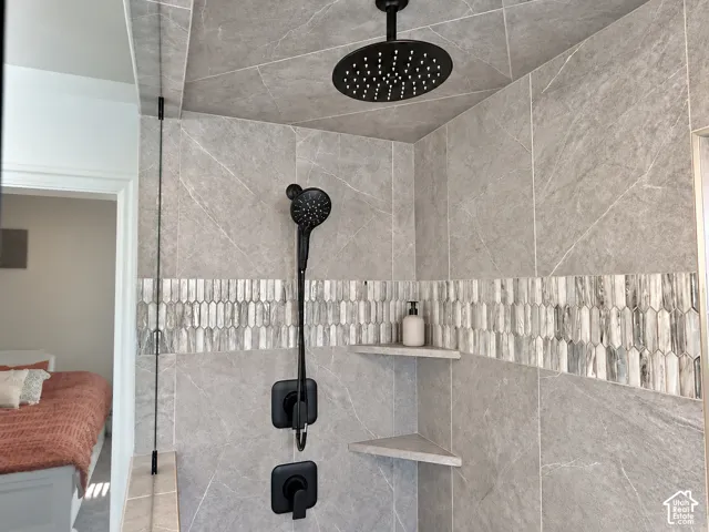 Walk-in shower featuring large-format stone-finish wall tiles, a decorative vertical-tiled accent border, ceiling-mounted rainfall showerhead, matte black handheld fixture, and integrated corner shelving