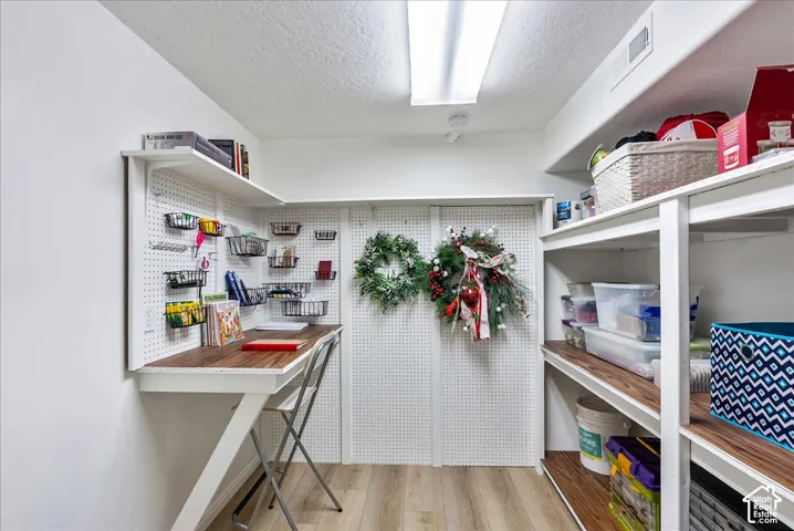 Dedicated storage room featuring wall-mounted pegboard organization, built-in wooden shelving, integrated workspace, and wood-finish flooring