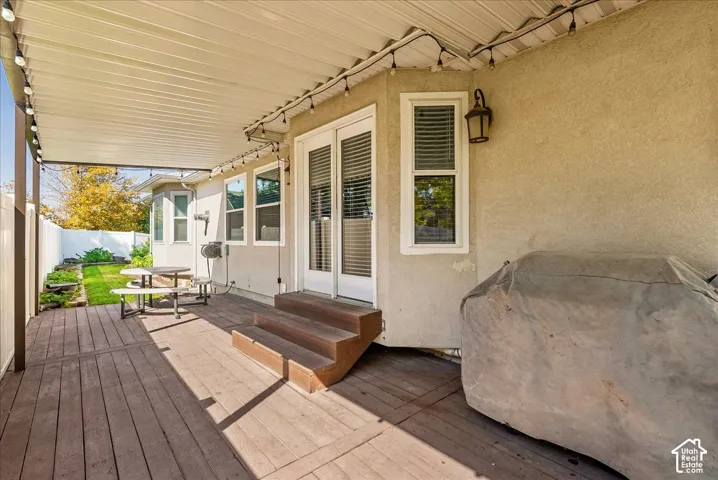 Covered deck featuring wood-finish decking, exterior wall-mounted lighting, metal roof covering, and glass-paned double doors with steps