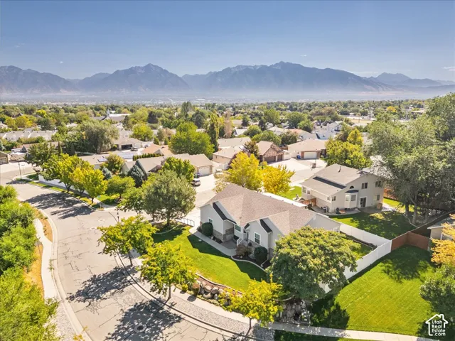 Aerial perspective of this residential property showcasing a manicured lawn, mature landscaping, and a driveway with concrete paving