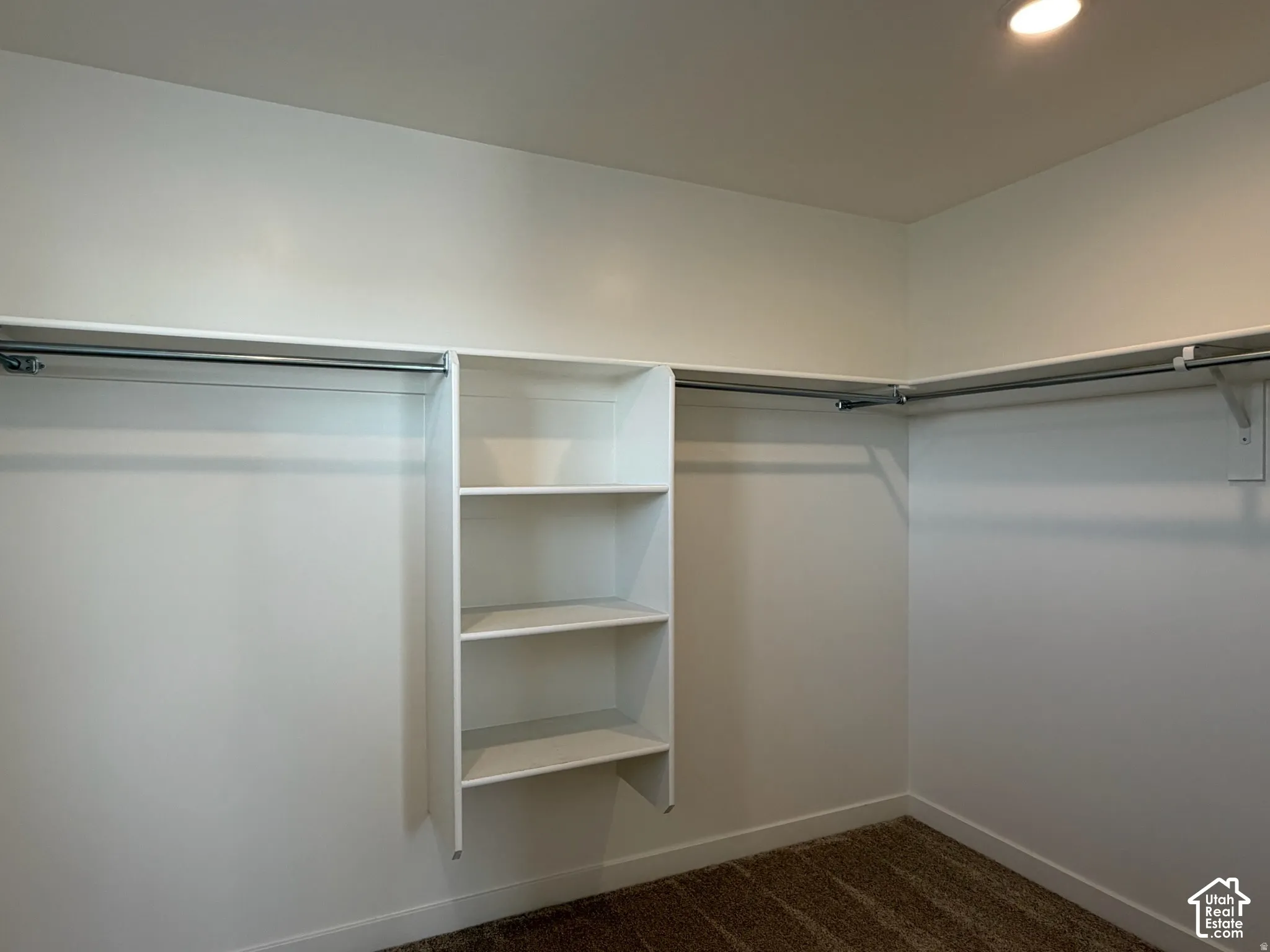Owner's wal-in closet with Recessed lighting illuminates the walk-in closet featuring white built-in shelving, two levels of hanging rods, and dark carpeting