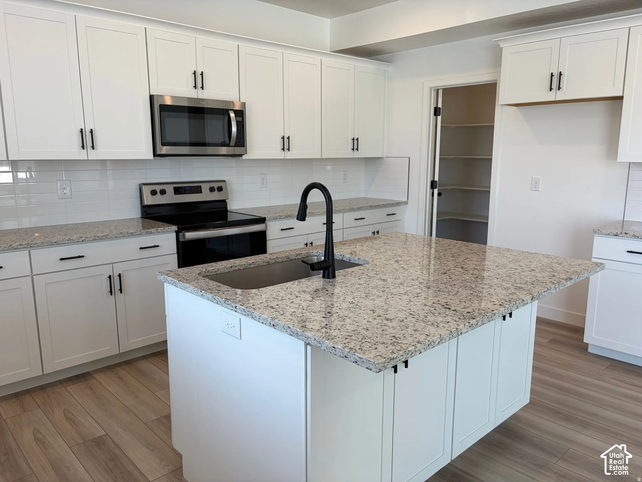White shaker-style cabinetry with matte black hardware, stone-finish countertops, stainless steel appliances, wood-finish flooring, and a walk-in pantry