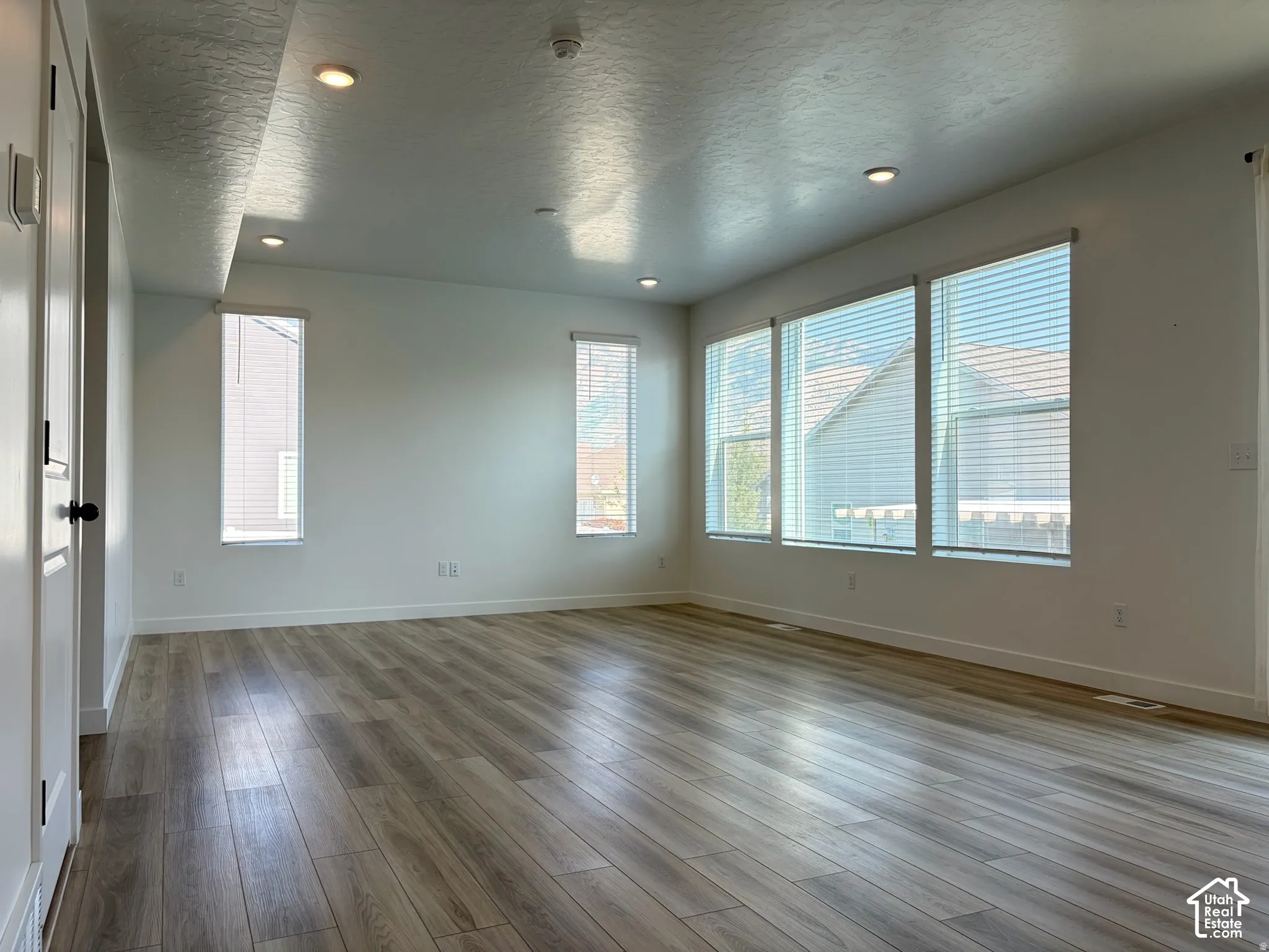 Recessed lighting, wood-finish flooring, multiple windows with blinds, and white painted walls