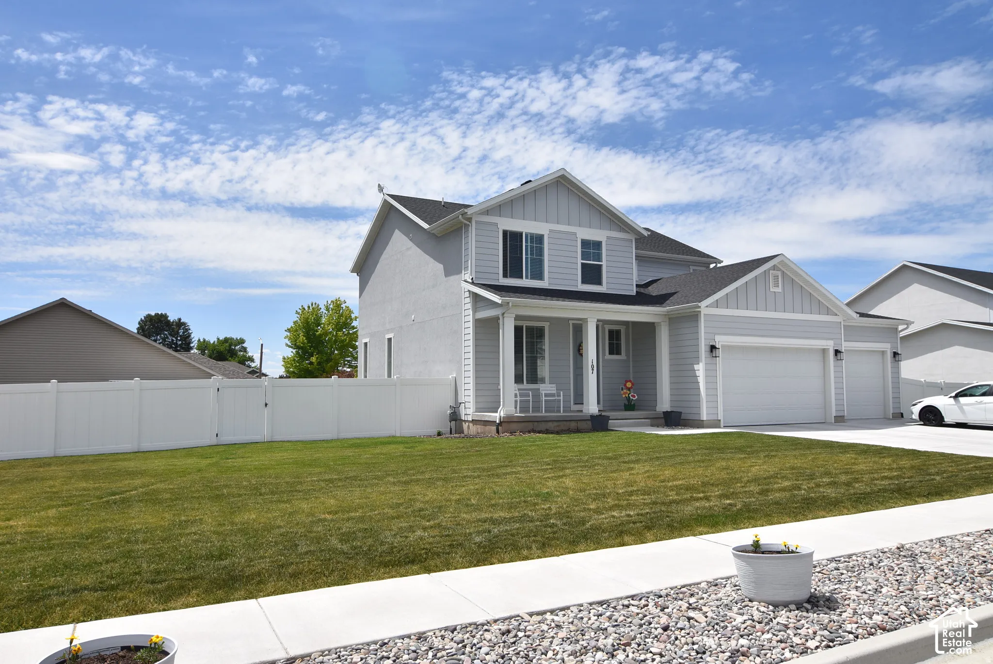 Two-story residence with a covered front porch, light gray siding, landscaped yard  and a 3-car attached garage