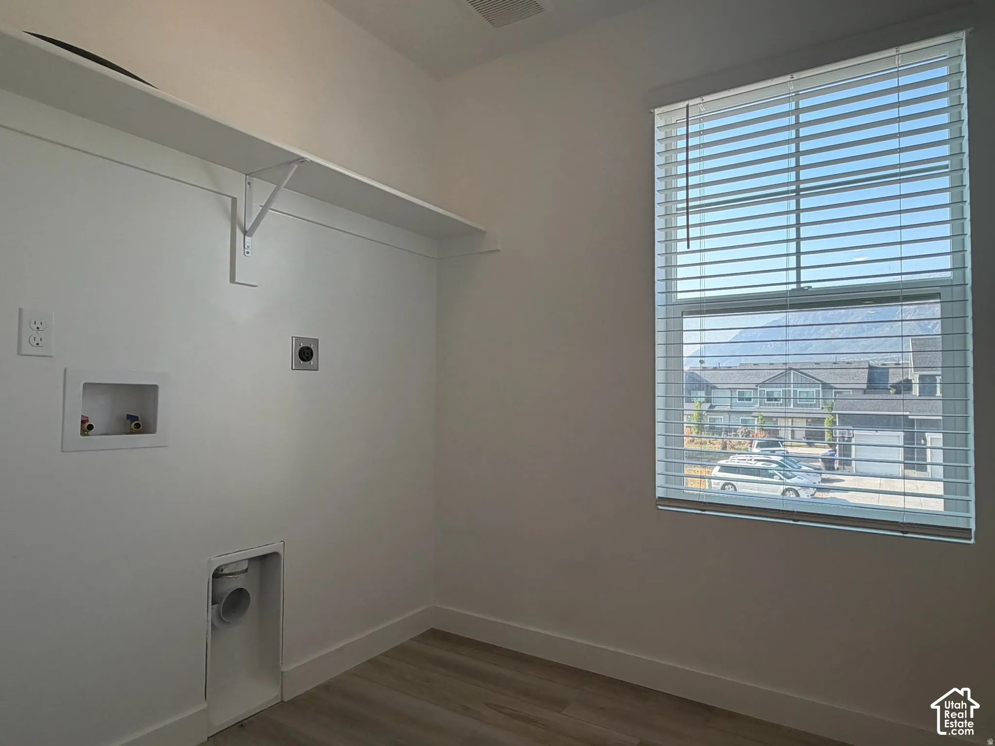 Dedicated laundry area featuring a wall-mounted shelf, utility hookups, wood-finish flooring, and a large window with blinds