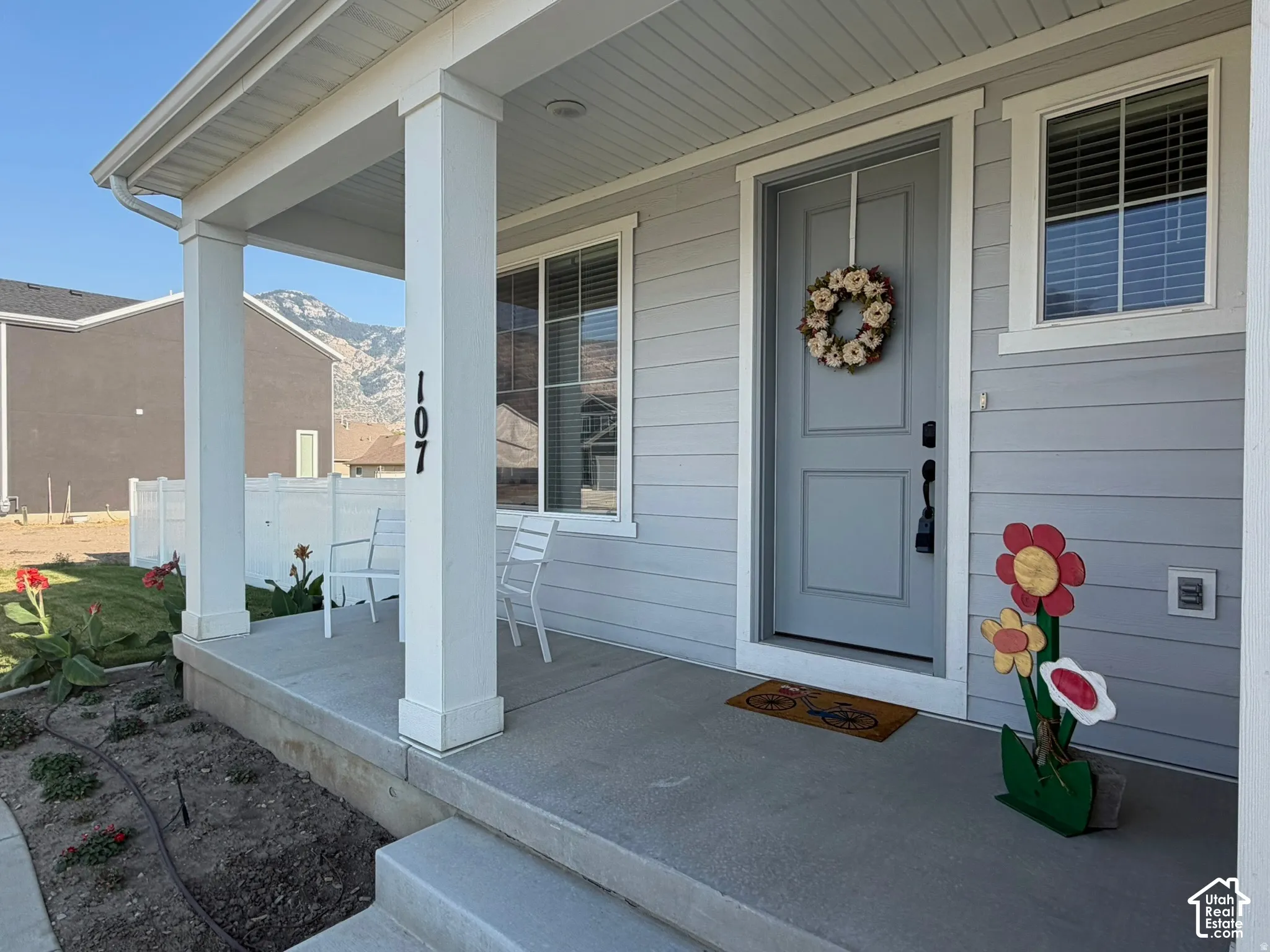 Covered front porch with two white support columns, light gray horizontal siding, a gray entry door, and a single window with white trim