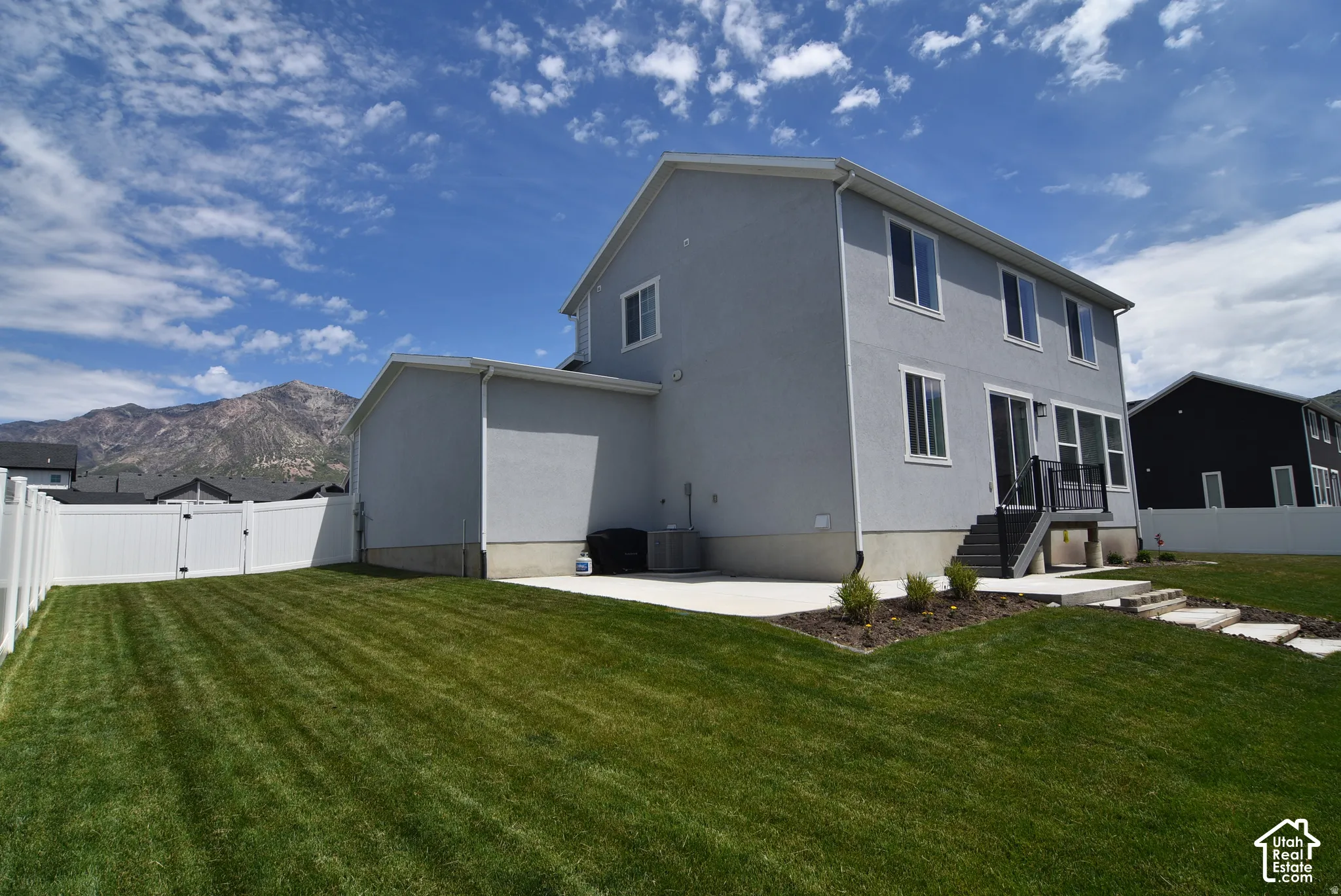 Stucco exterior with multiple windows, leading to a patio with stairs to a spacious lawn area.