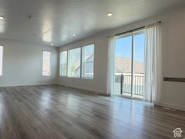 Spacious interior with wood-finish flooring, recessed lighting, multiple windows with blinds, and a glass sliding door leading to a balcony with black metal railings