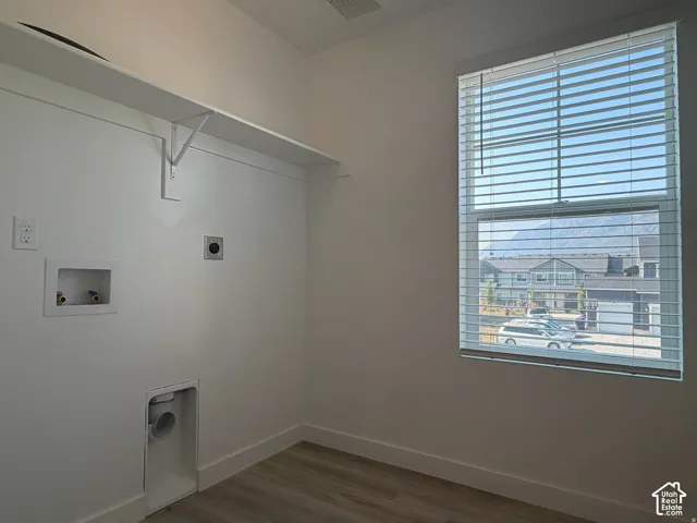 Dedicated laundry area featuring a wall-mounted shelf, utility hookups, wood-finish flooring, and a large window with blinds