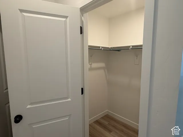 Bedroom # 2 closet White interior door with black hardware opening to a closet featuring wood-finish flooring, white walls, and built-in shelving with hanging rods
