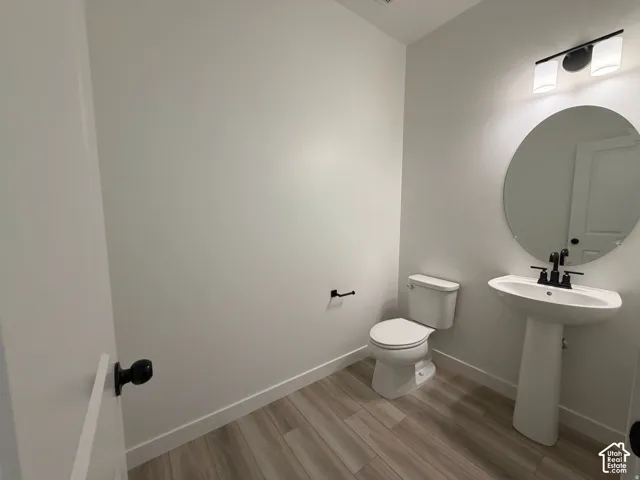 1/2 bath off entry with Pedestal sink with matte black faucet, wall-mounted oval mirror, and wood-finish flooring