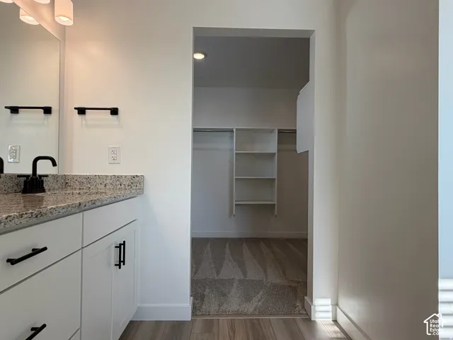 Owner's bathroom vanity with a speckled granite countertop, matte black hardware, and wood-finish flooring and entry into walk-in closet.