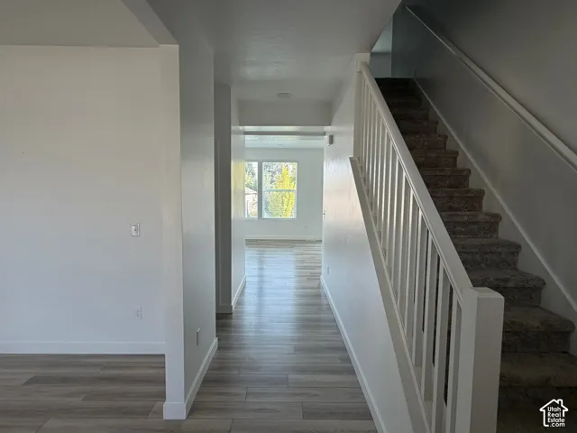 Expansive hallway with wood-finish flooring, recessed lighting, and a white baluster staircase with carpeted treads