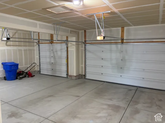 3- car garage with Two white garage doors with automatic openers, concrete flooring, and an attic access panel