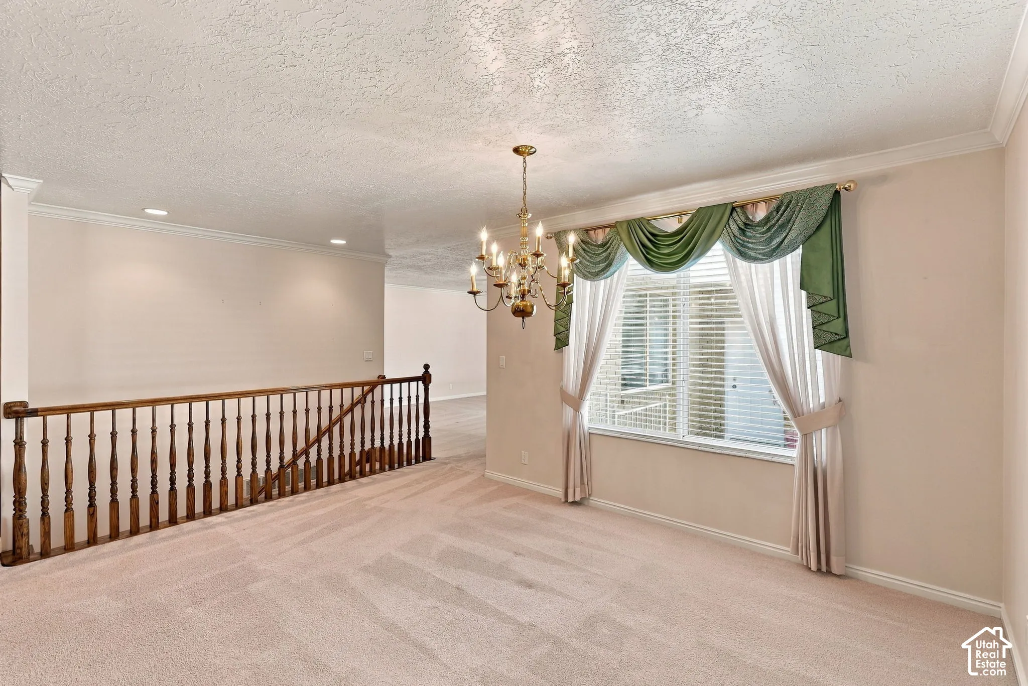 Brass chandelier, crown molding, baluster railing, recessed lighting, and a large window