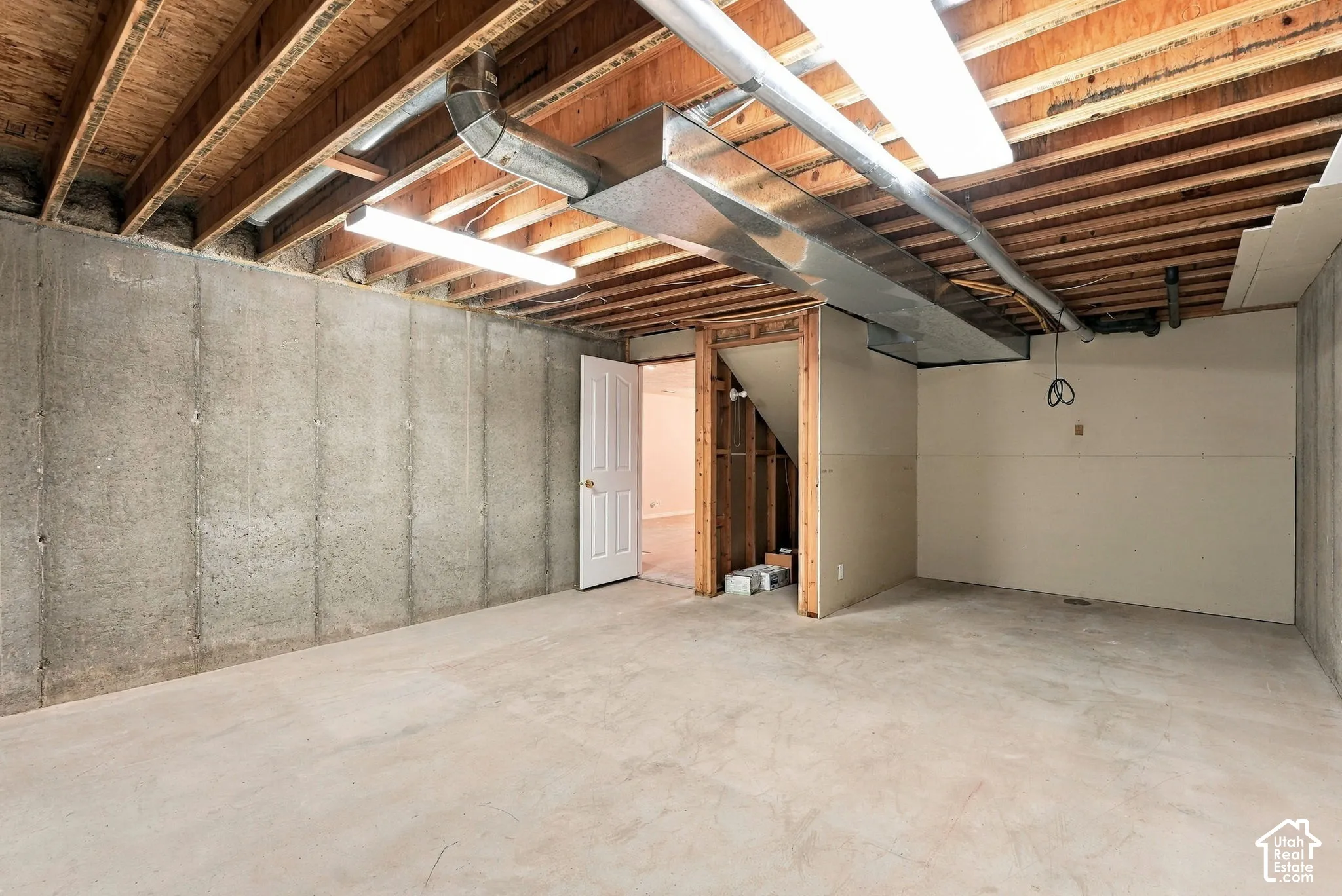 Unfinished basement space featuring concrete walls, exposed wood ceiling joists, and a concrete floor