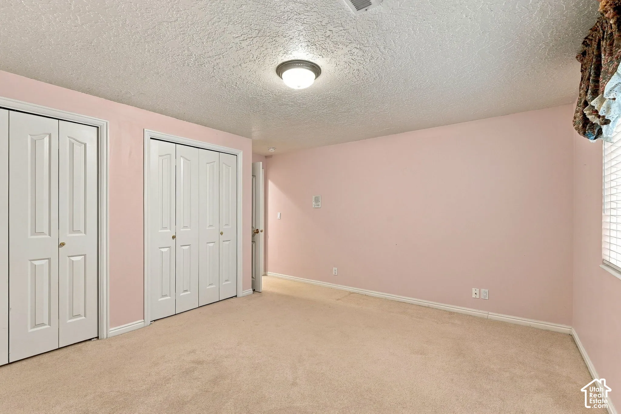 Wall-to-wall carpeting, two bi-fold door closets, recessed window with blinds, ceiling-mounted light fixture, and textured ceiling