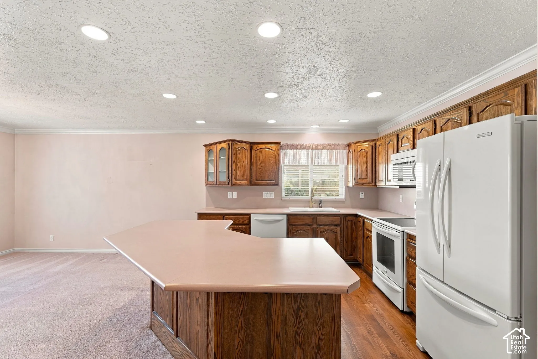 Kitchen featuring a central island, wood-finish cabinetry, white appliances, and recessed lighting