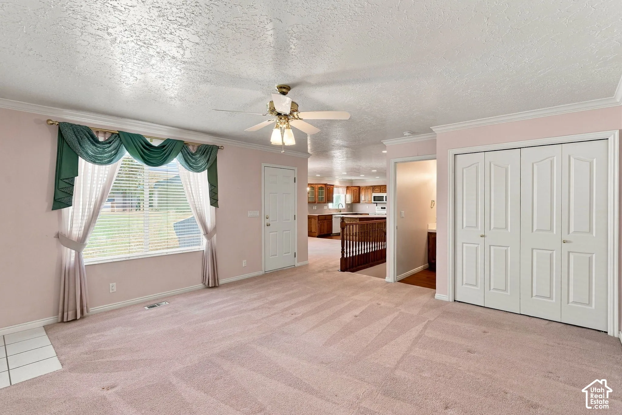 Spacious carpeted room featuring a ceiling fan with integrated lighting, a large window with blinds, and white bi-fold closet doors