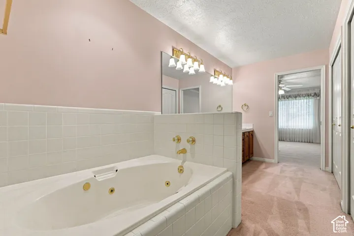 Built-in jetted tub surrounded by white tile, dual vanity with wood-finish cabinetry, gold-tone fixtures, and extensive wall mirror