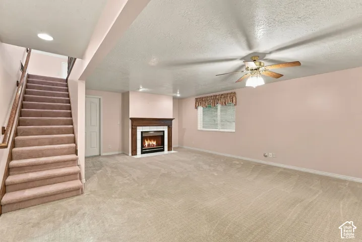 Carpeted living area featuring a central ceiling fan, window with blinds, and a built-in fireplace with a wood-finish mantel and white surround