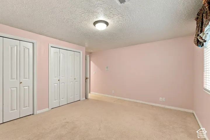 Wall-to-wall carpeting, two bi-fold door closets, recessed window with blinds, ceiling-mounted light fixture, and textured ceiling