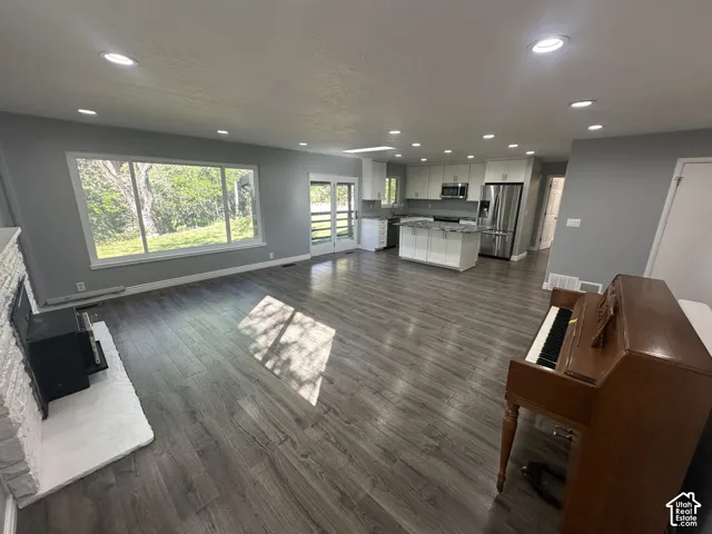 Open-concept layout with wood-finish flooring, white brick fireplace, and recessed lighting