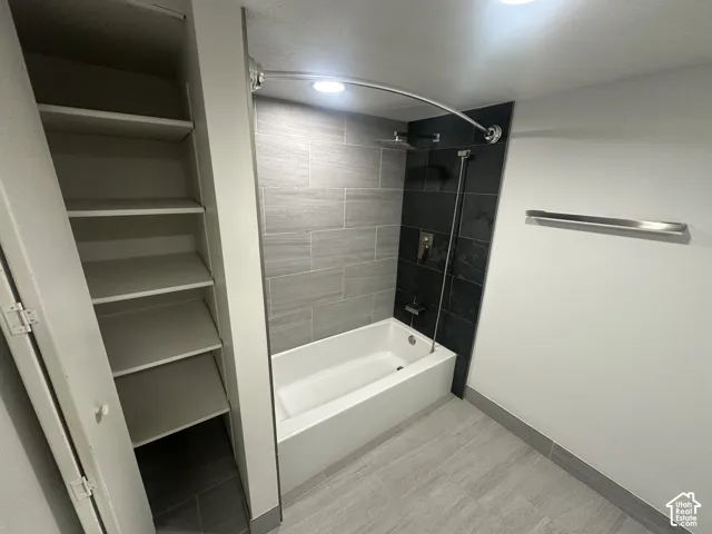 Full bathtub with overhead shower, two-tone tiled shower surround, recessed lighting, and built-in shelving