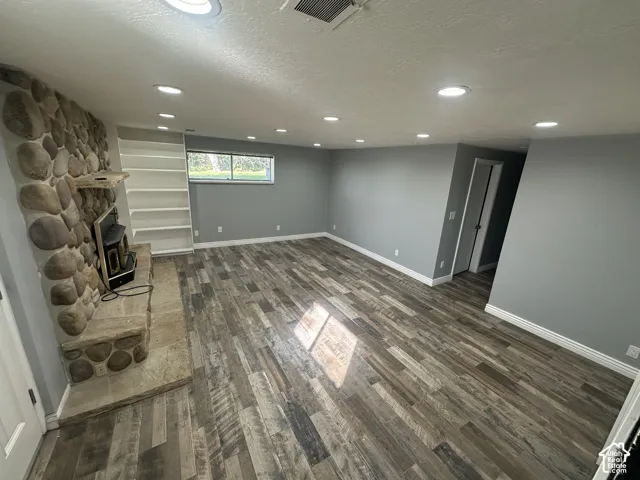 Stone fireplace with hearth, built-in shelving, wood-finish flooring, recessed lighting, and a window