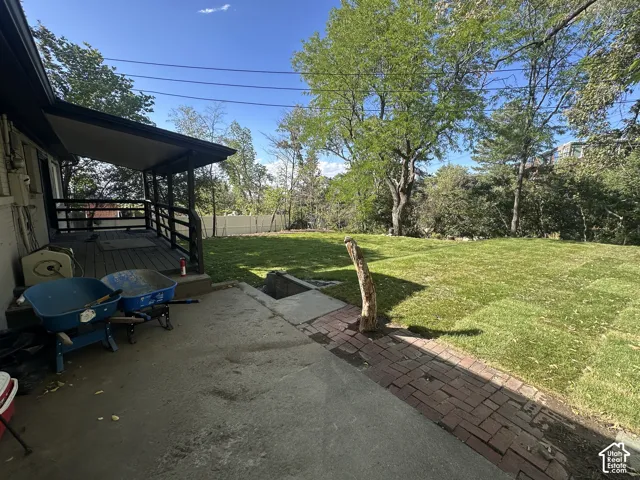Expansive backyard featuring a manicured lawn, mature trees, a concrete patio, and a covered porch with wood railings