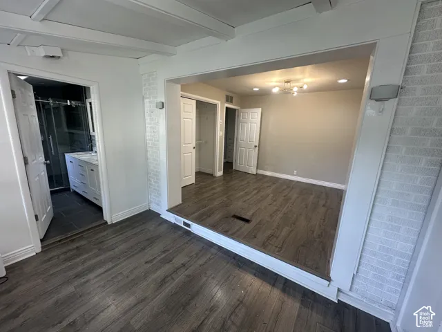 Wood-finish flooring, exposed ceiling beams, white brick accent wall, modern vanity with dual sinks, and a glass-enclosed shower