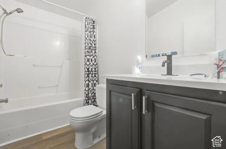 White shower-tub combination, dark wood-finish vanity with white countertop, integrated sink, and wood-finish flooring