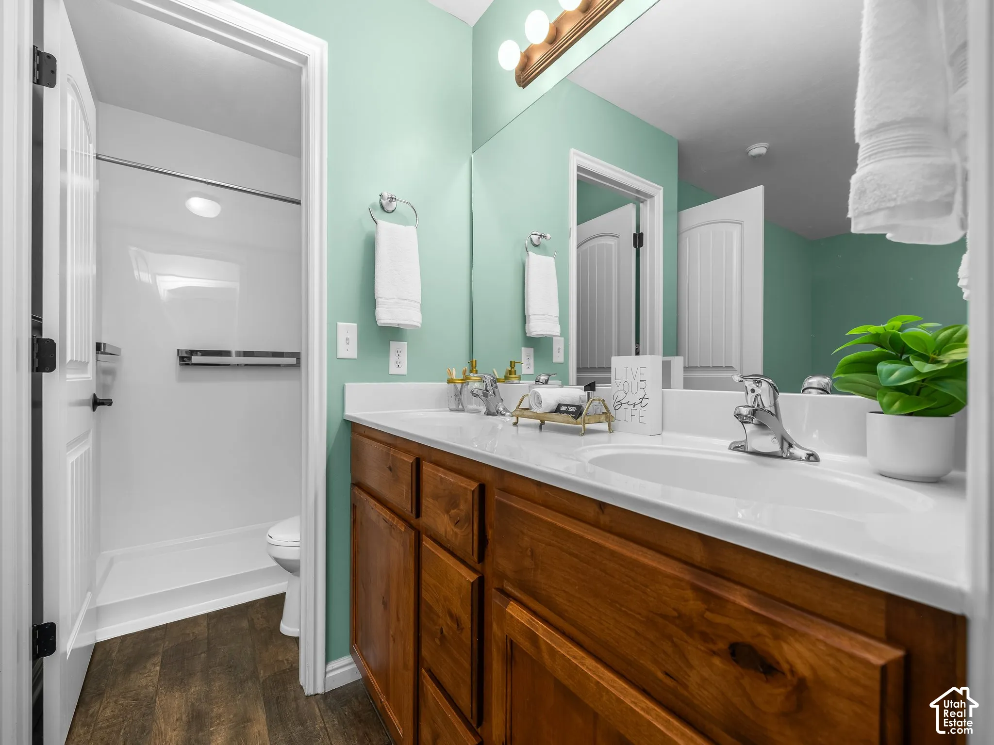 Wood-finish flooring, wood cabinetry with paneled doors, white countertop, integrated sink, and a walk-in shower with a white surround