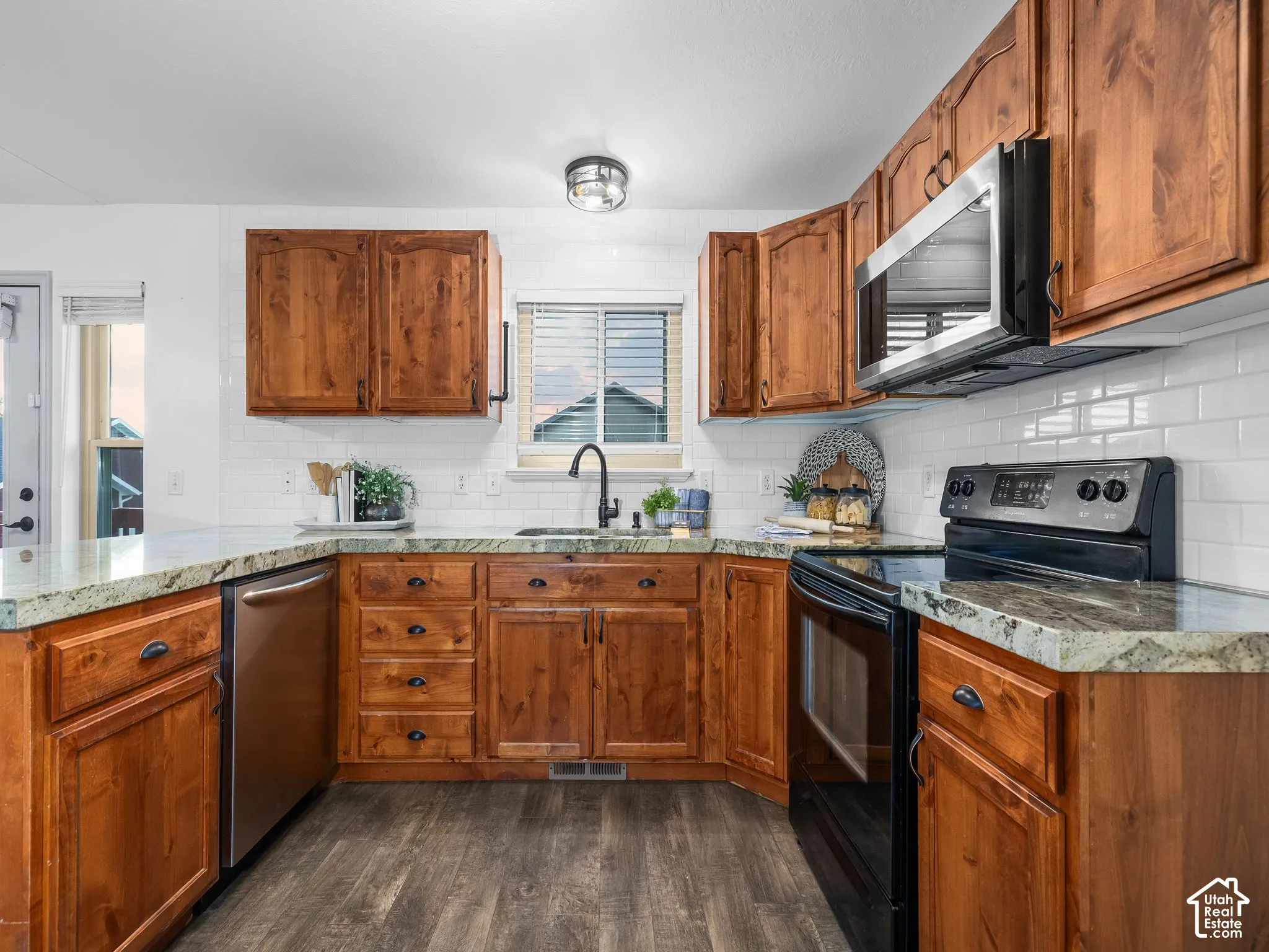 Warm wood cabinetry with brushed hardware frames this kitchen featuring stainless steel appliances, white subway tile backsplash, granite countertops, and dark wood-finish flooring throughout