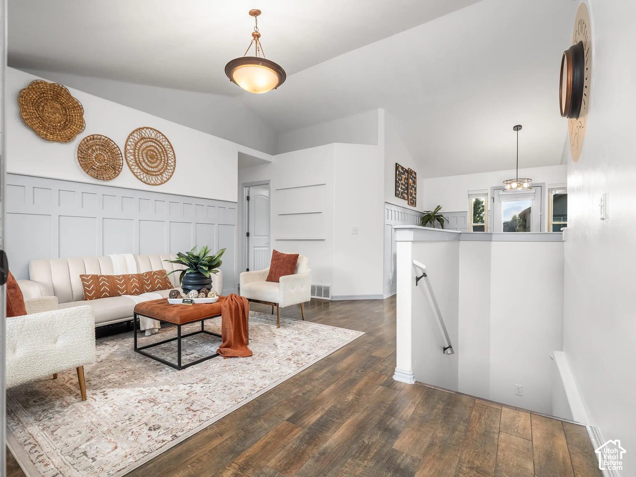 Vaulted ceiling with an overhead light fixture, board and batten accent wall, wood-finish flooring, and a staircase with a white railing