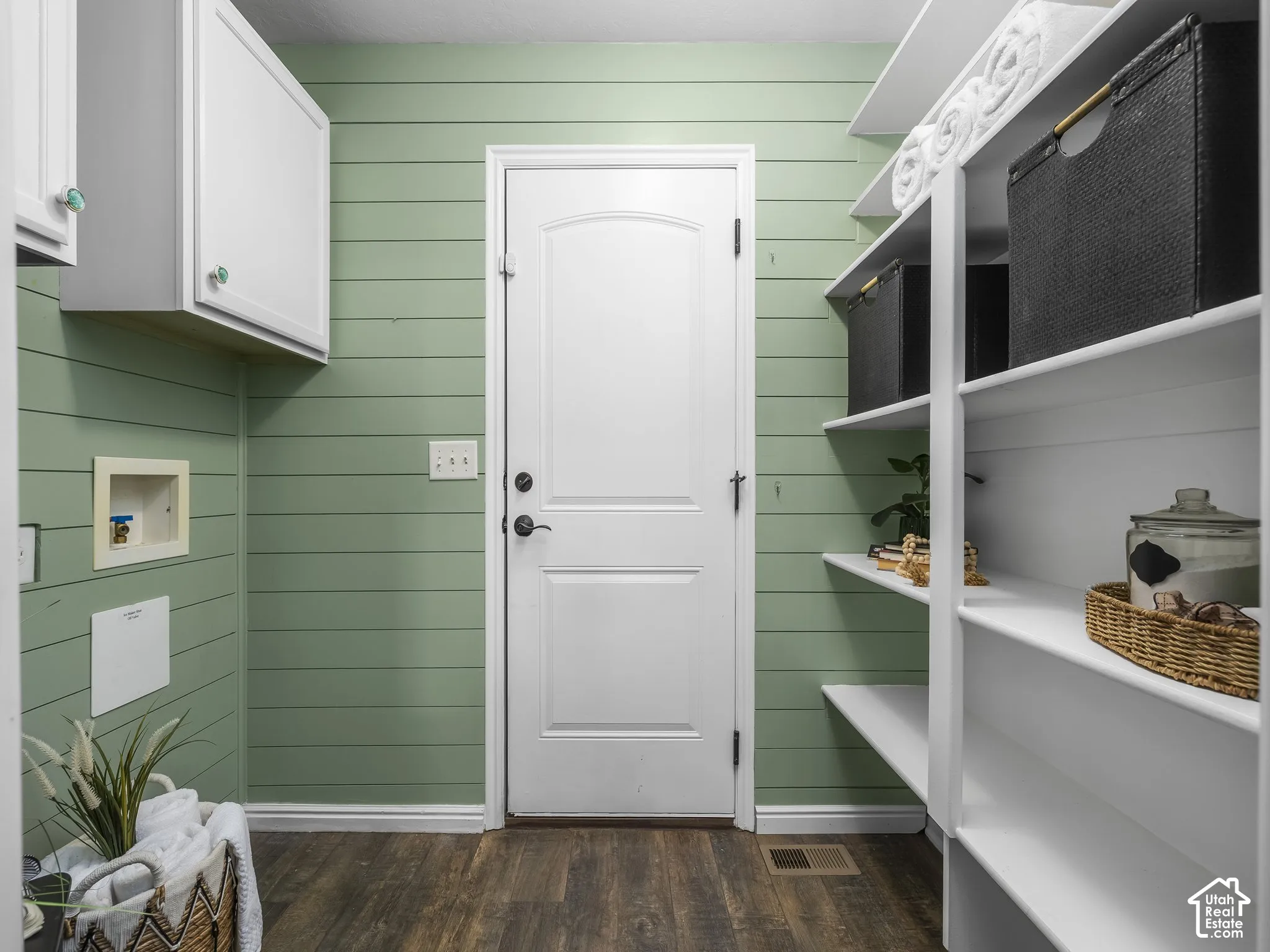 Bright mudroom featuring soft green shiplap walls, white panel door entry, wood-finish flooring, and custom white built-in shelving with open storage