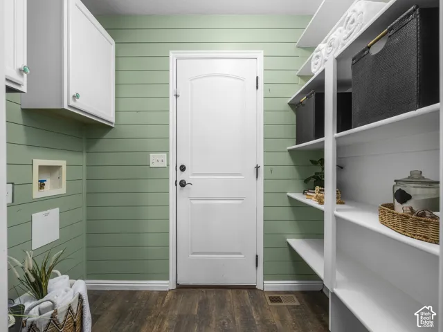 Bright mudroom featuring soft green shiplap walls, white panel door entry, wood-finish flooring, and custom white built-in shelving with open storage