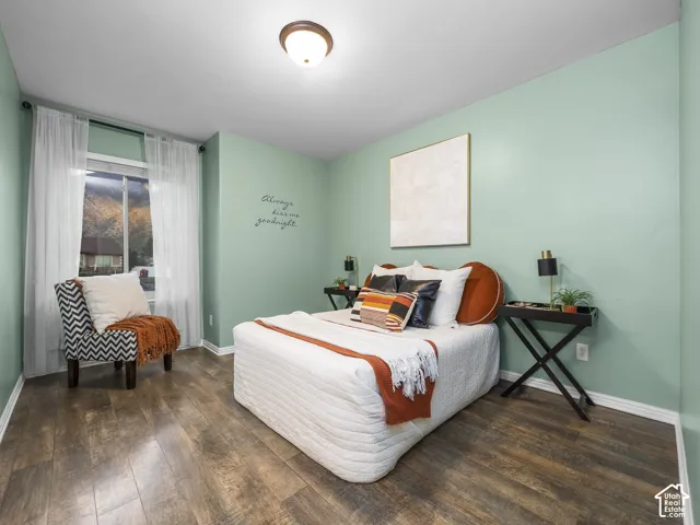 Serene bedroom retreat featuring soft sage-green walls, wood-finish flooring throughout, and abundant natural light from a generous window with sheer curtains