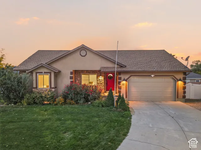 Stucco exterior with stone accents, covered entry, attached garage, and landscaping with mature plantings