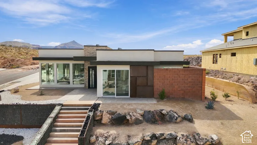 Modern flat-roof architecture featuring stucco and stone-clad exterior with large fixed-pane windows and a sliding glass door