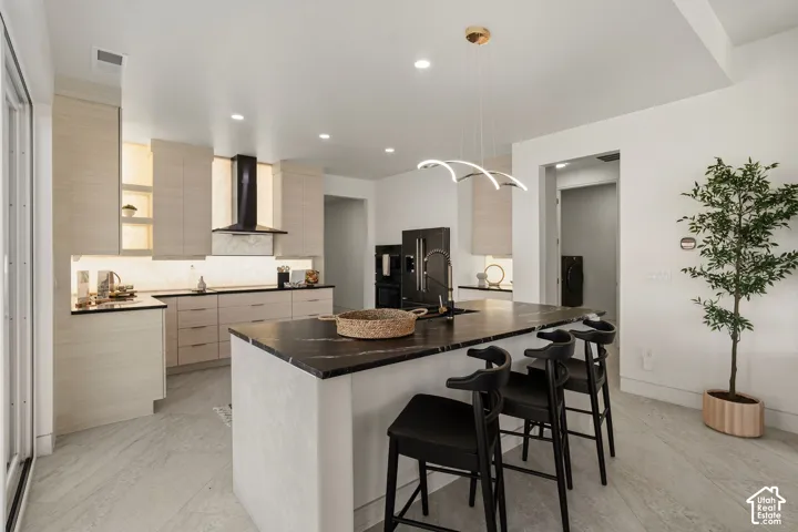 Kitchen featuring a large island with dark stone countertop, light wood-finish cabinetry, recessed lighting, and a contemporary pendant light fixture