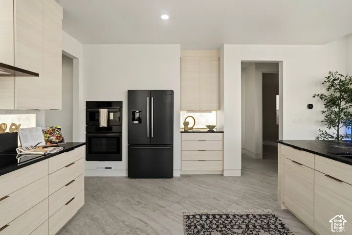 Light wood-tone cabinetry with linear hardware, black countertops, integrated double ovens, and a black French door refrigerator