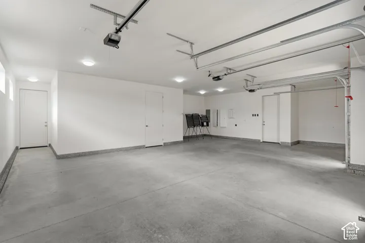 Concrete flooring, white painted walls, multiple overhead lighting fixtures, exposed garage door mechanisms, and a service door
