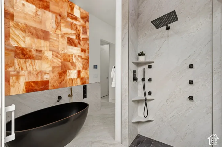Freestanding soaking tub with matte black fixtures, an illuminated stone accent wall, and a tiled walk-in shower with multiple body sprayers and a rainfall showerhead