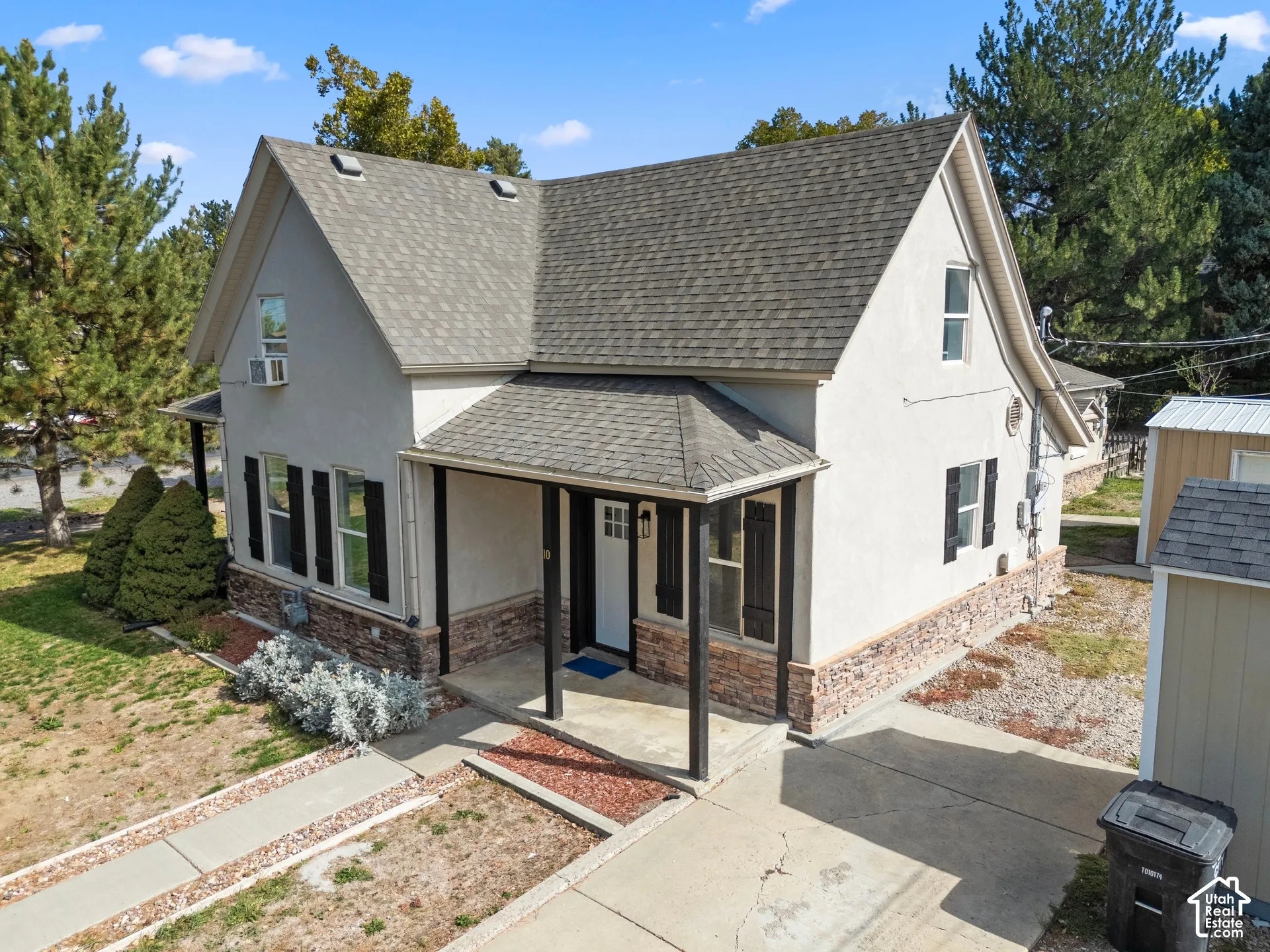 Stucco exterior with stone veneer accents, covered front porch, asphalt shingle roof, and exterior shutters