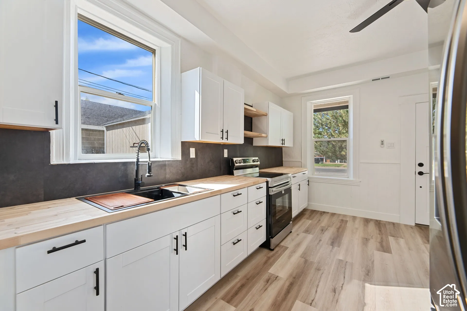 Main House New Kitchen with White shaker cabinetry with black hardware, wood-finish countertops, dark tile backsplash, stainless steel range, and wood-finish flooring