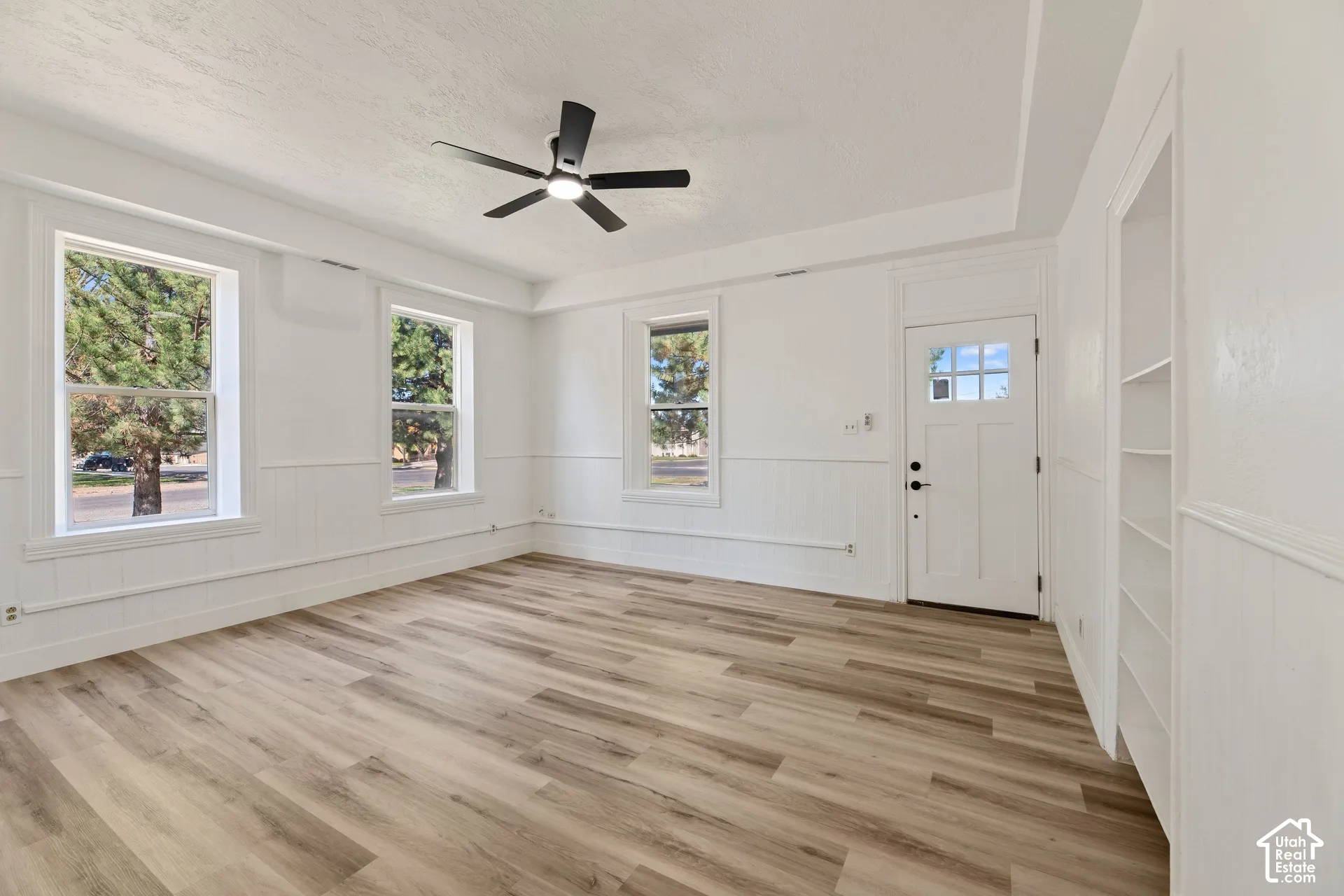 Main House Living Room with New LVP Wood-finish flooring, multiple windows, white paneling, built-in shelving, and a ceiling fan